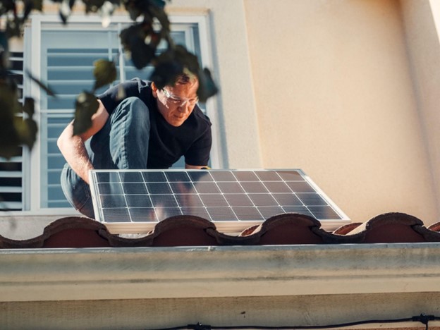 A man installing a small solar panel to his home’s roof