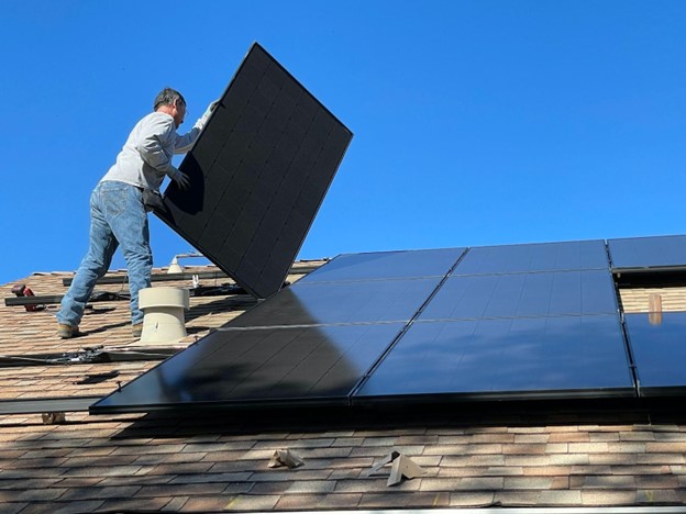 A man lifting a solar panel into place on a rooftop